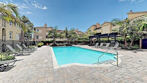 Una piscina amb gandules i ombrel·les, envoltada d'edificis i palmeres.