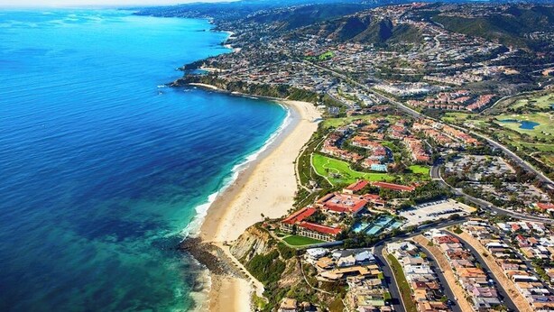 Vista aèria d'una ciutat costanera amb una platja, zones residencials i un camp de golf.