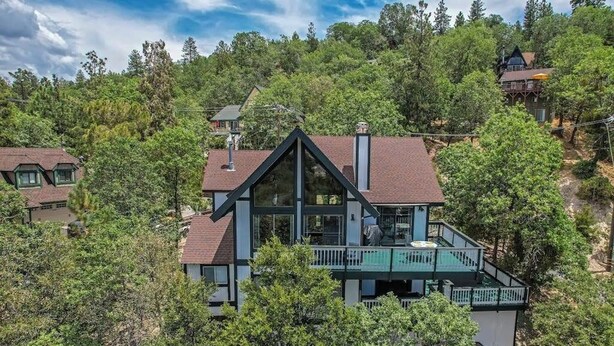 A large house with a prominent balcony, surrounded by dense forest. - 3BR/2.5BA home with views, yard, BBQ, game room, fireplace & EV charger (Lake Arrowhead)