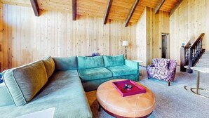 A wooden interior with a sectional sofa, a patterned armchair, and a round coffee table. - 3BR/2.5BA home with views, yard, BBQ, game room, fireplace & EV charger (Lake Arrowhead)