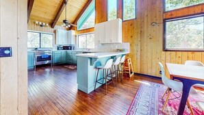 A spacious kitchen with wooden beams, a large island with bar stools, and a dining area with a table and chairs. - 3BR/2.5BA home with views, yard, BBQ, game room, fireplace & EV charger (Lake Arrowhead)