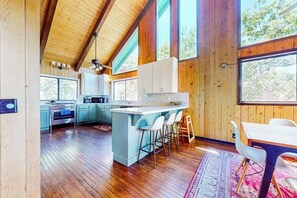 A spacious kitchen with wooden beams, a large island with bar stools, and a dining area with a table and chairs. - 3BR/2.5BA home with views, yard, BBQ, game room, fireplace & EV charger (Lake Arrowhead)