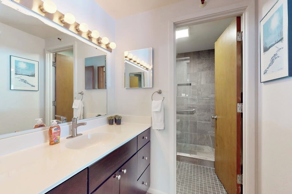 A bathroom with a large mirror, vanity, and a shower area.