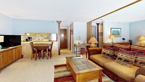 Un salon comprenant un canapé, une table basse et un téléviseur. Il y a également un coin cuisine avec une table à manger et des chaises.