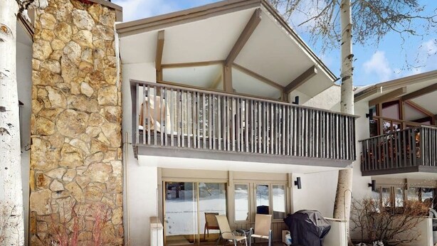 Un bâtiment à deux étages doté d’une façade en pierre, d’un balcon avec une balustrade en bois et d’un espace extérieur aménagé et couvert pour s’asseoir.