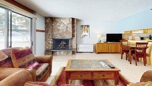 Un salon avec une cheminée en pierre, un canapé agrémenté de coussins à motifs, une table basse et un téléviseur.