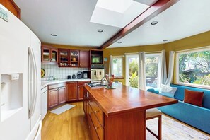 A kitchen with wooden cabinets, a central island, and a window overlooking greenery. - Charming, Single-Level Home w/ Fast WiFi, Gas Fireplace, & a Furnished Patio (Santa Barbara)
