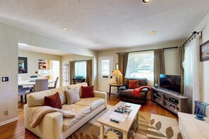 A living room with a sofa, a coffee table, a TV, and a dining area in the background. - Charming, Single-Level Home w/ Fast WiFi, Gas Fireplace, & a Furnished Patio (Santa Barbara)
