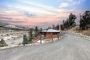 Ein rundes Gebäude mit verschneietem Dach, umgeben von einem Zaun und Bäumen, am Ende einer Straße.