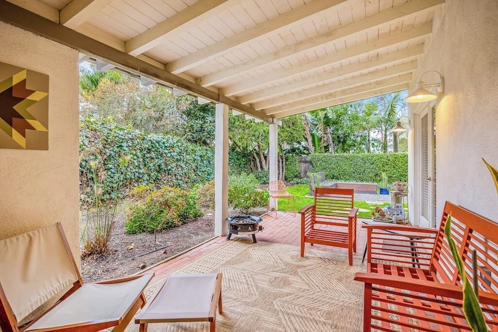 A covered patio with wooden furniture, a fire pit, and a view of a garden.