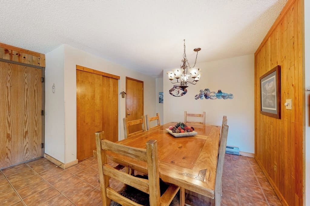 Un comedor con una mesa de madera, sillas, una araña y paredes de madera.