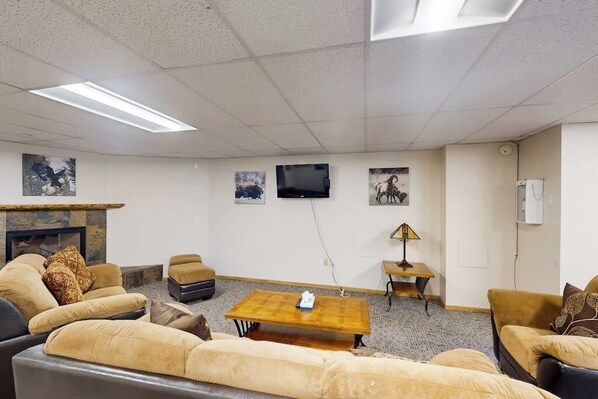A living room with sofas, a coffee table, a fireplace, a flat-screen TV, and artwork on the walls.