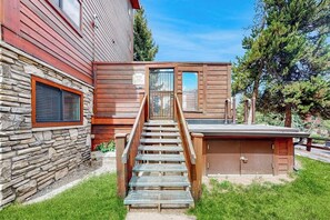 A wooden staircase leading to a covered outdoor area with a stone wall and a window with blinds.