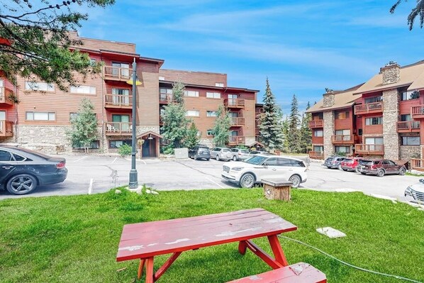 A multi-story building with balconies, a parking lot, and a picnic table in the foreground.