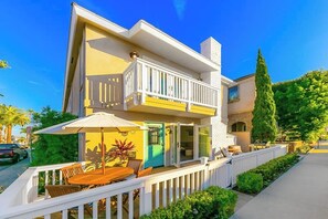 Ein zweistöckiges Haus mit einem Balkon, einer Terrasse mit Tisch und Stühlen und einem gepflegten Garten.