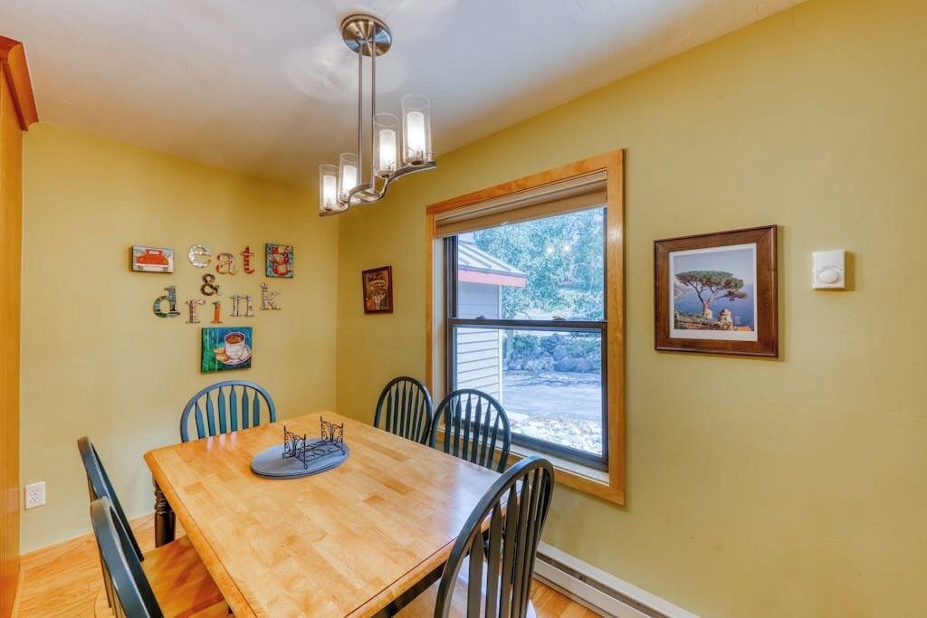 A dining room with a wooden table, black chairs, a chandelier, and a window with a view.