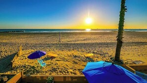 Une plage avec du sable baigné de soleil, un palmier et deux parasols.