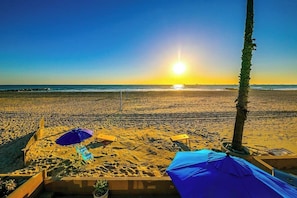 Ein Strand mit sonnigem Sand, einer Palme und zwei Sonnenschirmen.