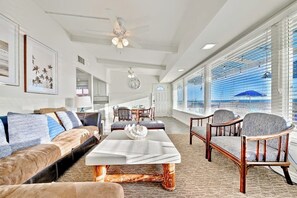 Ein geräumiges Wohnzimmer mit einer Couch, Sesseln, einem Couchtisch und Blick durch große Fenster.