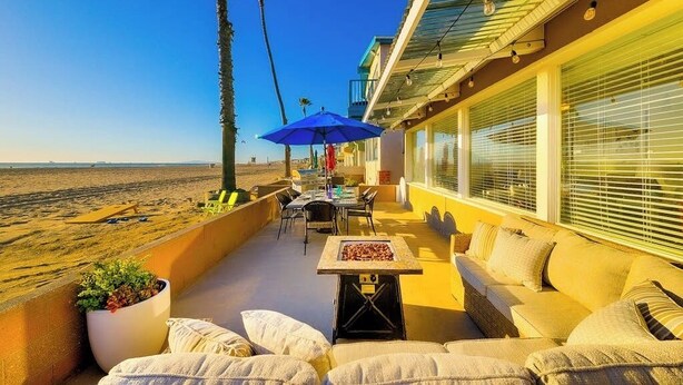 Un balcon avec vue sur la plage, une table avec des chaises, un parasol bleu et un canapé.