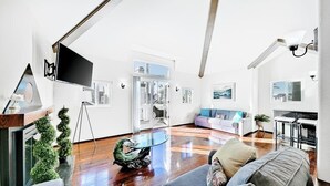 Ein modernes Wohnzimmer mit einem großen Flachbildfernseher, einem Glastisch und einem grauen Sofa.