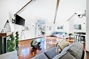 Ein modernes Wohnzimmer mit einem großen Flachbildfernseher, einem Glastisch und einem grauen Sofa.