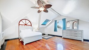 Ein Schlafzimmer mit schrägen Wänden, einem Bett, einem Schminktisch und einem Oberlicht.