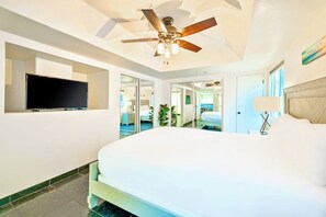 Ein Hotelzimmer mit einem großen Bett, einem Deckenventilator, einem Flachbildfernseher und Blick auf den Poolbereich.
