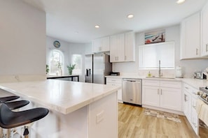 A modern kitchen with white cabinets, a stainless steel refrigerator, and a dishwasher. - Classic dog-friendly home with fast WiFi, full kitchen, & A/C - near beaches (Newport Beach)