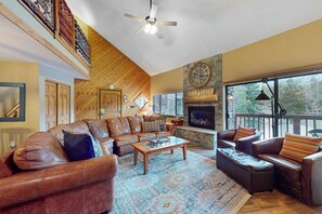 A spacious living room with leather sofas, a fireplace, and a large window overlooking a deck. - Cozy 3rd-floor condo w/ hot tubs, fireplace, balcony, gym, & views (Breckenridge)