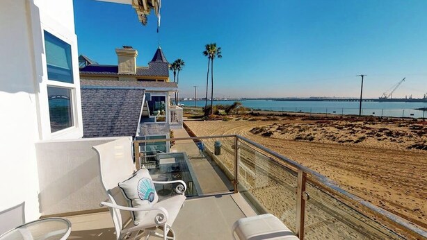 Un balcone con tavolo e sedie in vetro che si affaccia su una spiaggia e un molo.