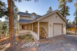 Ein zweistöckiges Haus mit überdachter Veranda, Garage und einem Holzstapel.