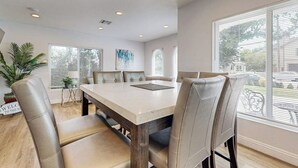 Uma sala de jantar com uma mesa grande e cadeiras, um vaso de planta e vista para o exterior.