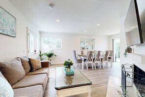 A modern living room with a sofa, a glass coffee table, a fireplace, and a dining area with chairs. - Dual homes with 2 full kitchens, fast WiFi, fireplace, & patio - dog-friendly (Newport Beach)