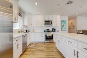 A modern kitchen with white cabinets, stainless steel appliances, and a wooden floor. - Dual homes with 2 full kitchens, fast WiFi, fireplace, & patio - dog-friendly (Newport Beach)
