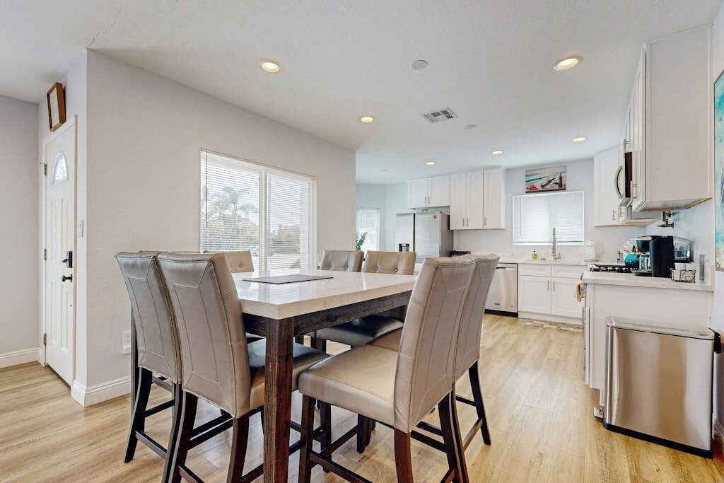 A modern kitchen with white cabinets, a dining table with chairs, and a refrigerator.