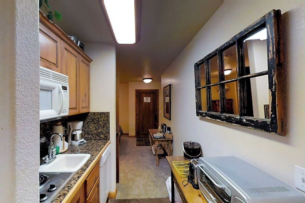A narrow hallway leading to a kitchen with wooden cabinets, a microwave, and a coffee maker.