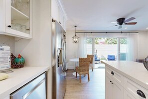 Eine moderne Küche mit weißen Schränken, ein Essbereich mit Korbstühlen und einem Deckenventilator.