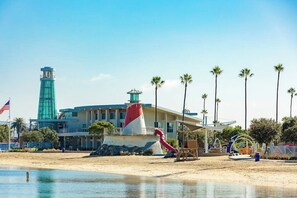 Ein Strandhotel mit Leuchtturm, Palmen und einem Spielplatz.