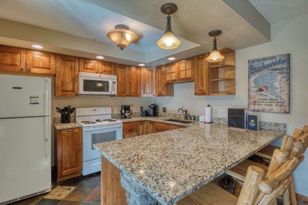A kitchen with wooden cabinets, a granite countertop, a white refrigerator, a stove, and a microwave.