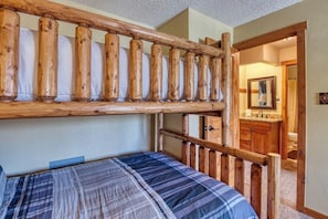 Ein Stockbett mit Holz Kopfteil, ein Badezimmer mit Waschbecken und Spiegel sowie eine Tür zu einem weiteren Raum.