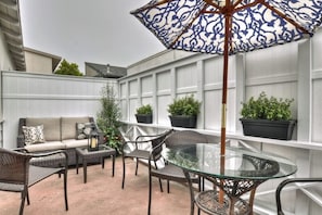 Eine Terrasse mit Korbmöbeln, einem Glastisch und Topfpflanzen.