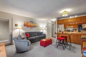 A compact living space with a sofa, a chair, a small table, a kitchen area, and a bar stool. - Ski-In/Ski-Out from this Cozy, Family-Friendly Mountain Condo - Walk to Town (Breckenridge)