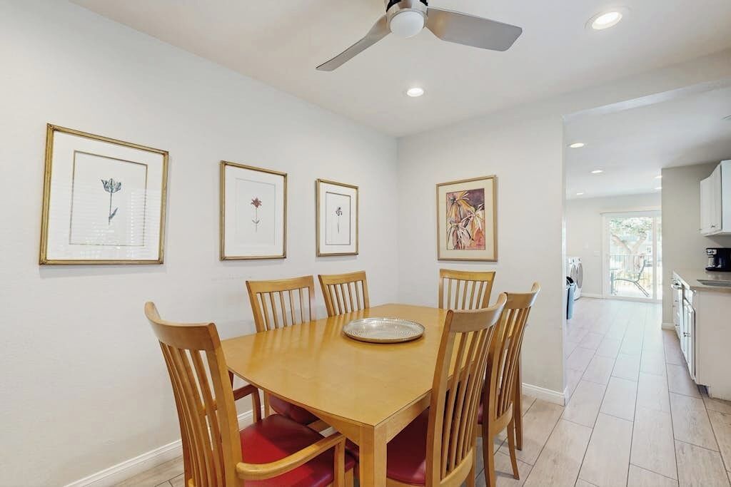 A dining area with a wooden table and chairs, framed artwork on the walls, and a ceiling fan.