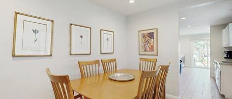 A dining area with a wooden table and chairs, framed artwork on the walls, and a ceiling fan.