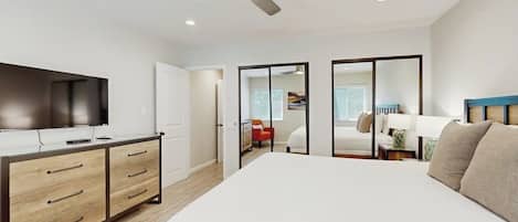 A bedroom with a bed, a desk with drawers, a ceiling fan, and a television.