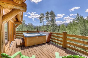 Eine Holzterrasse mit Whirlpool, Holzwertung und einer Bergkulisse im Hintergrund.
