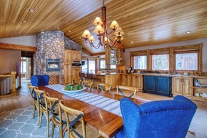 Eine geräumige Küche mit Kamin aus Stein, Holzschränken und einem großen Esstisch mit Stühlen.