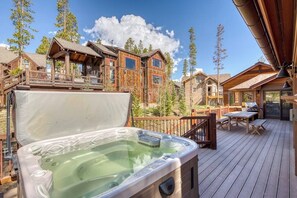 Ein Whirlpool auf einer Holzterrasse mit Blick auf Holzhütten und Bäume.