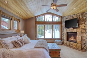 Ein Schlafzimmer mit einem großen Bett, einem Kamin aus Stein, einem Fernseher und einem Deckenventilator.
